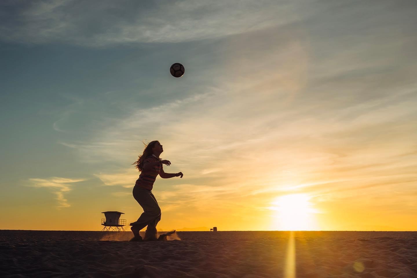 A person playing with a soccer ball on the beach at sunset